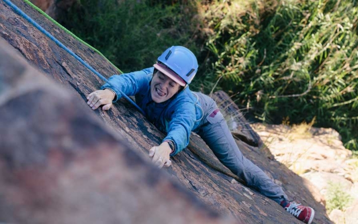 a person climbing a rock wall makes a silly face at the camera
